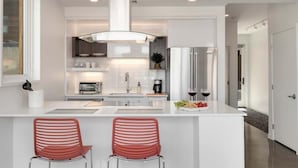 A modern kitchen with a central island, two red chairs, stainless steel appliances, and a large window. - Modern Elegance on Linden – Walk/Bike Everywhere! (Fort Collins)