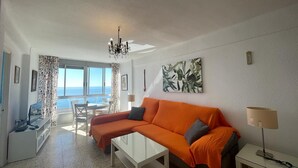 A bright living room with a white sofa, a glass coffee table, and a view of the sea through large windows. - TERRASOL FRONTAL AL MAR ANTILLAS 8 (Torre del Mar)
