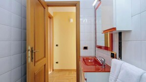 Un pasillo estrecho que conduce a un baño con lavamanos y espejo.