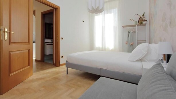 Un dormitorio con cama, armario, mesita de noche y ventana con cortinas.
