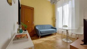 Una habitación con piso de madera, un sofá azul, una mesa blanca y una silla blanca.