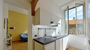 Cocina compacta con encimera negra, armarios blancos y ventana con vistas a un tejado de tejas.