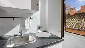 Una cocina moderna con un lavamanos de acero inoxidable, salpicadero de azulejos blancos y una ventana con vistas a tejados de teja.