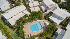 An aerial view of a residential area with multiple houses, a central swimming pool, and surrounding greenery.