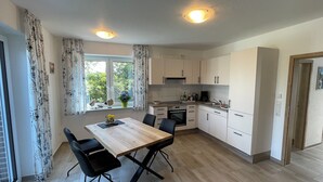 Ett modernt kök med en matplats, med ett träbord och stolar, ett fönster med gardiner och utsikt över grönområden utanför.