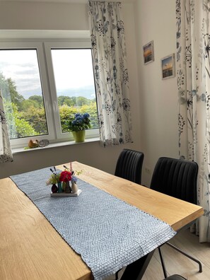 Un comedor con una mesa de madera, un camino de mesa azul con textura y una planta en maceta con flores.