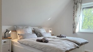 A bedroom with a white bed, two bedside tables, a window with curtains, and a ceiling light. - Country house Hassel 1  (Wiefelstede)