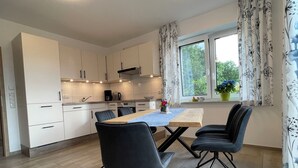 A modern kitchen with white cabinets, a dining table with two chairs, and a window with curtains. - Country house Hassel 1  (Wiefelstede)