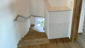 A staircase with wooden steps leading to a landing with a white wall and a small white cabinet. - Country house Hassel 1  (Wiefelstede)