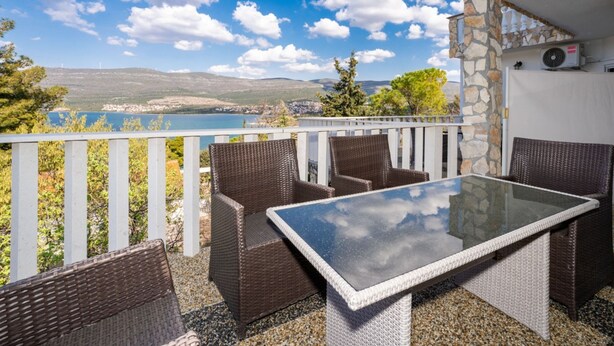 Un balcón con mobiliario de mimbre y una mesa de vidrio, con vistas a un lago y montañas.
