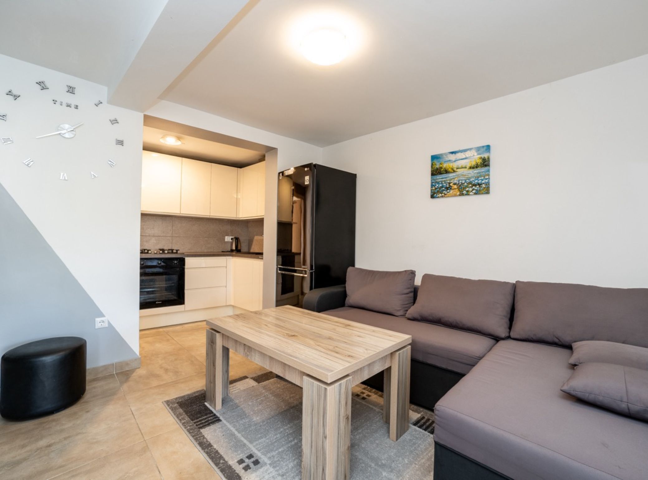 A modern living room with a wooden coffee table, a sofa, and a kitchen area with cabinets and appliances.