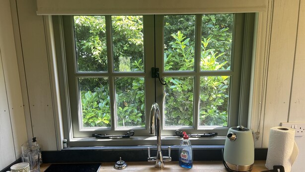 A kitchen with a sink, faucet, and window overlooking greenery. - Cozy Cabin Retreat in Bedford (Bedford)