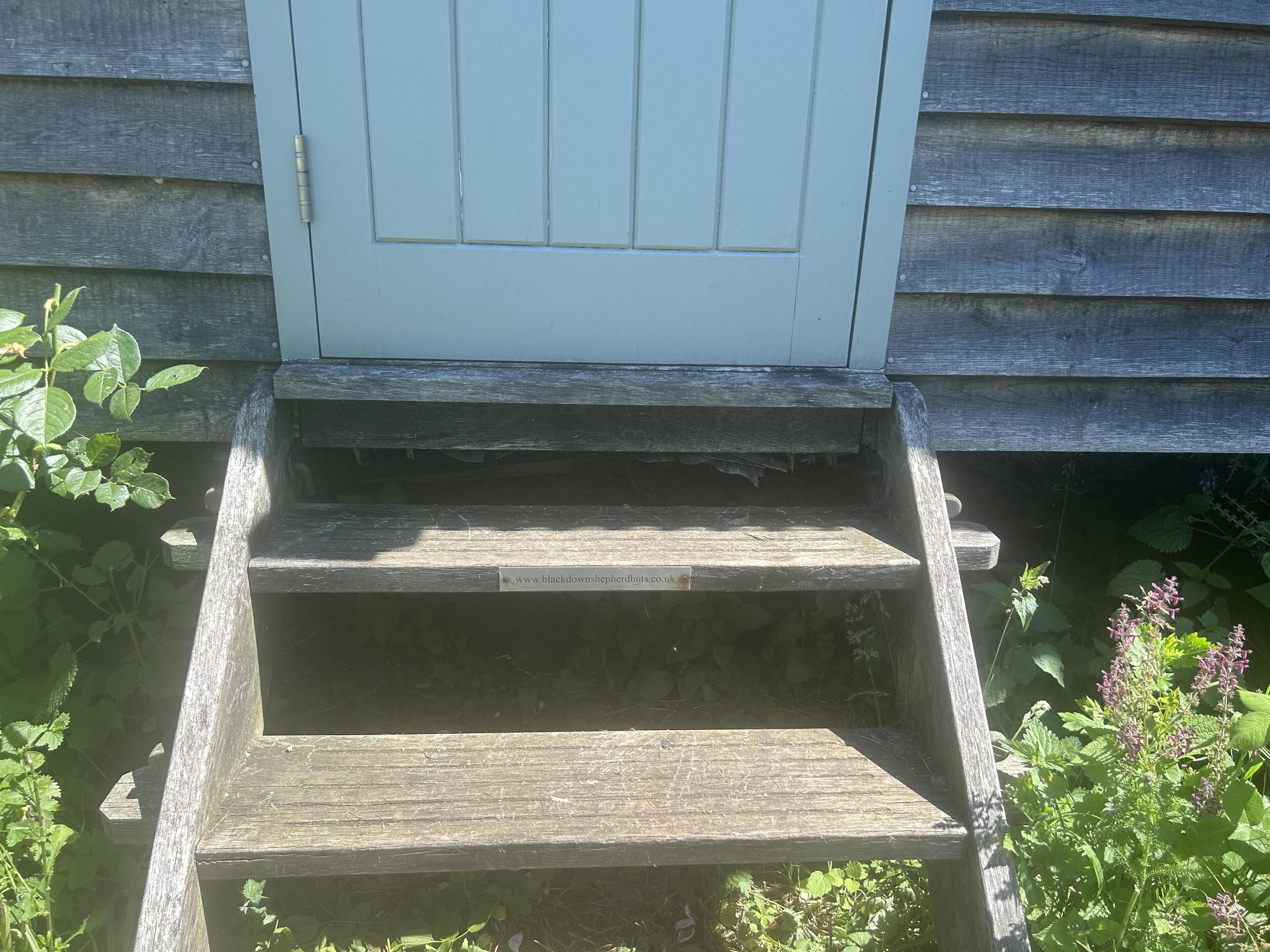 A set of wooden steps leading to a door with a sign above it.