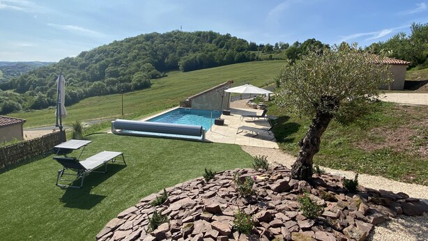 A swimming pool with a patio area, a stone wall, and a view of a hilly landscape. - Gite TT Confort Proche Millau / Roquefort VUE Panoramique Piscine Chauffee (SAINT-VICTOR-ET-MELVIEU)