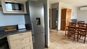 A modern kitchen with a built-in microwave, a stainless steel refrigerator, and a water dispenser. There is a dining area with a wooden table and chairs. - Gite TT Confort Proche Millau / Roquefort VUE Panoramique Piscine Chauffee (SAINT-VICTOR-ET-MELVIEU)