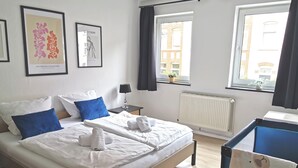 Una camera d'albergo con due letti, un termosifone, una finestra con tende e quadri appesi al muro.