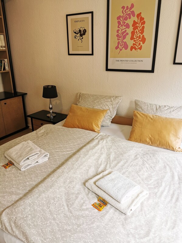 Una habitación de hotel con una cama bien hecha, una mesita de noche con lámpara y dos cuadros enmarcados en la pared.