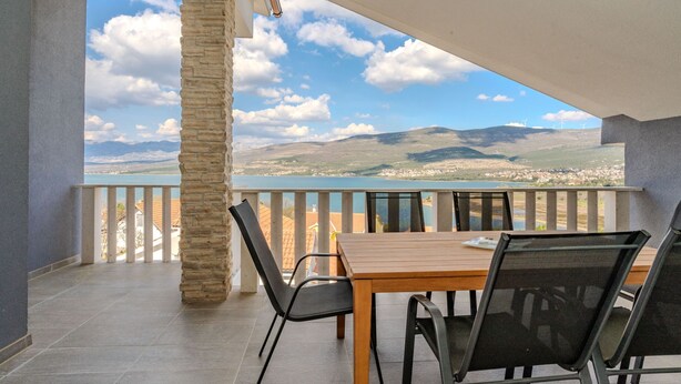 Un balcon avec une table et des chaises en bois, offrant une vue panoramique sur un lac et des montagnes.