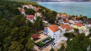 Une vue aérienne d’un village côtier avec des maisons, une piscine et une vue sur la mer et les montagnes.