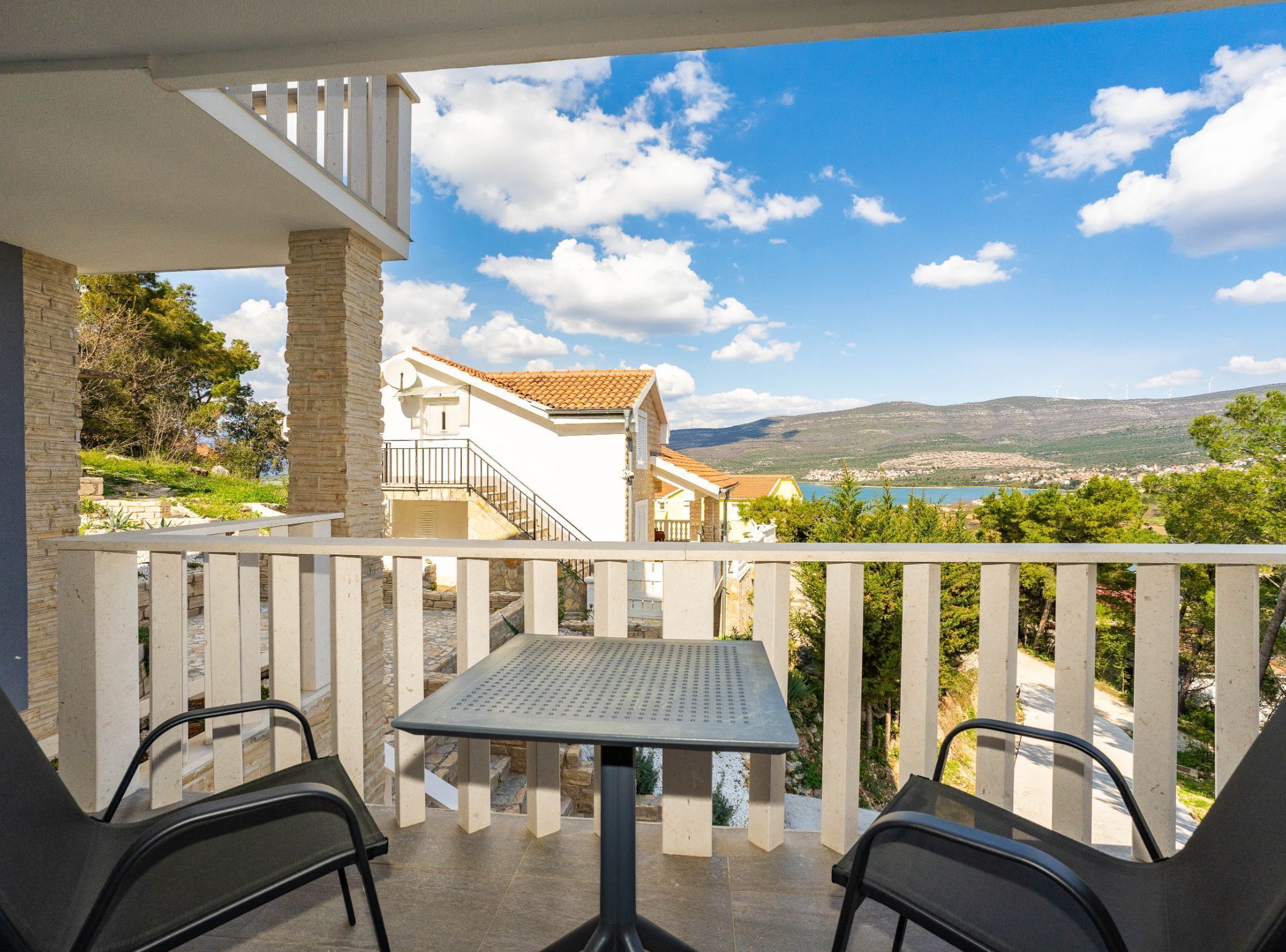 A balcony with a table and chairs, overlooking a scenic view of a town and mountains.