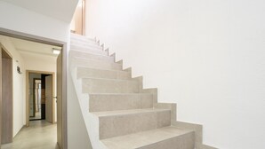 Un escalier moderne avec des marches de couleur beige et une rampe en bois, menant à une pièce dotée d’une porte et d’un luminaire mural.