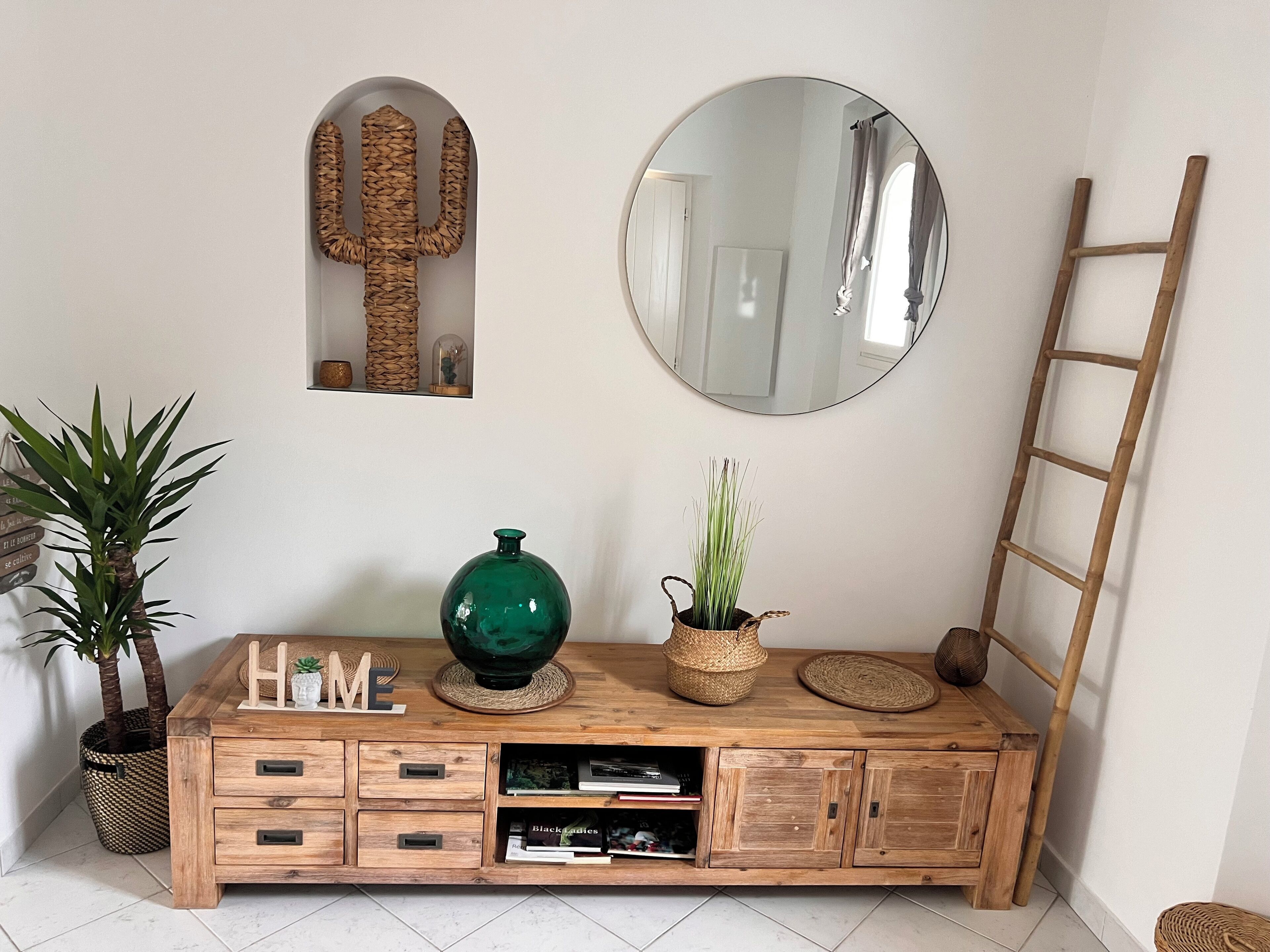 A wooden console table with a green vase, a potted plant, and a mirror above it.
