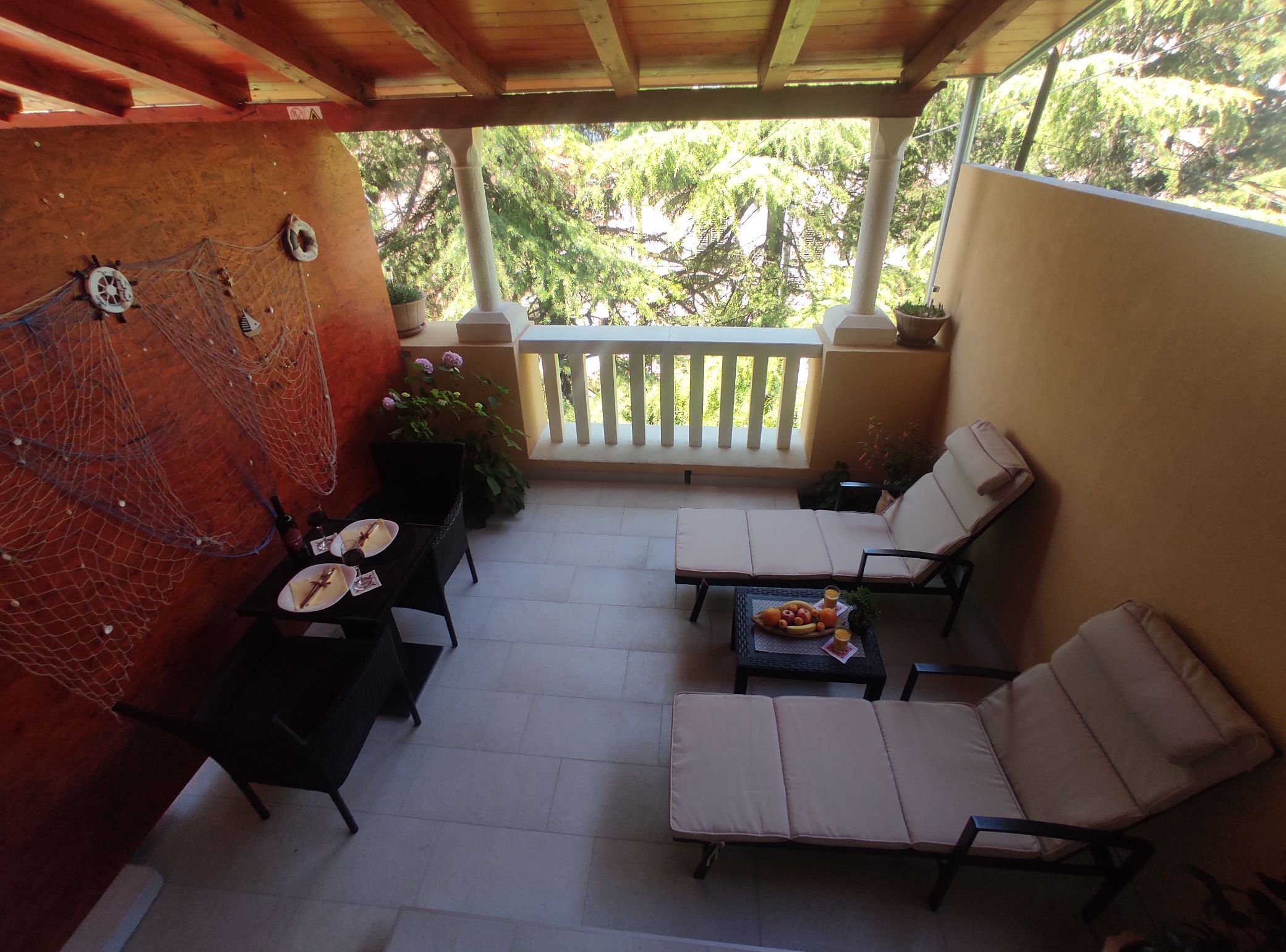 A covered patio with two lounge chairs, a table with a fruit bowl, and a decorative wall with a net and hats.