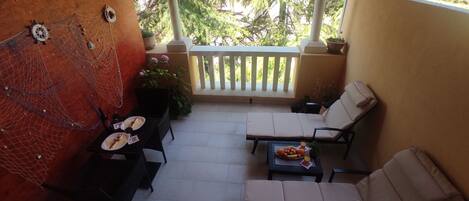 A covered patio with two lounge chairs, a table with a fruit bowl, and a decorative wall with a net and hats.