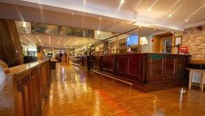 A spacious lobby with a wooden floor, a reception desk, and a bar area. - Weston Manor (Bicester)