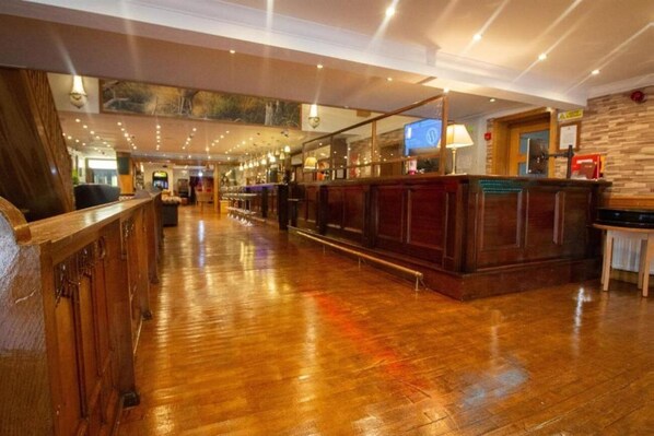 A spacious lobby with a wooden floor, a reception desk, and a bar area. - Weston Manor (Bicester)