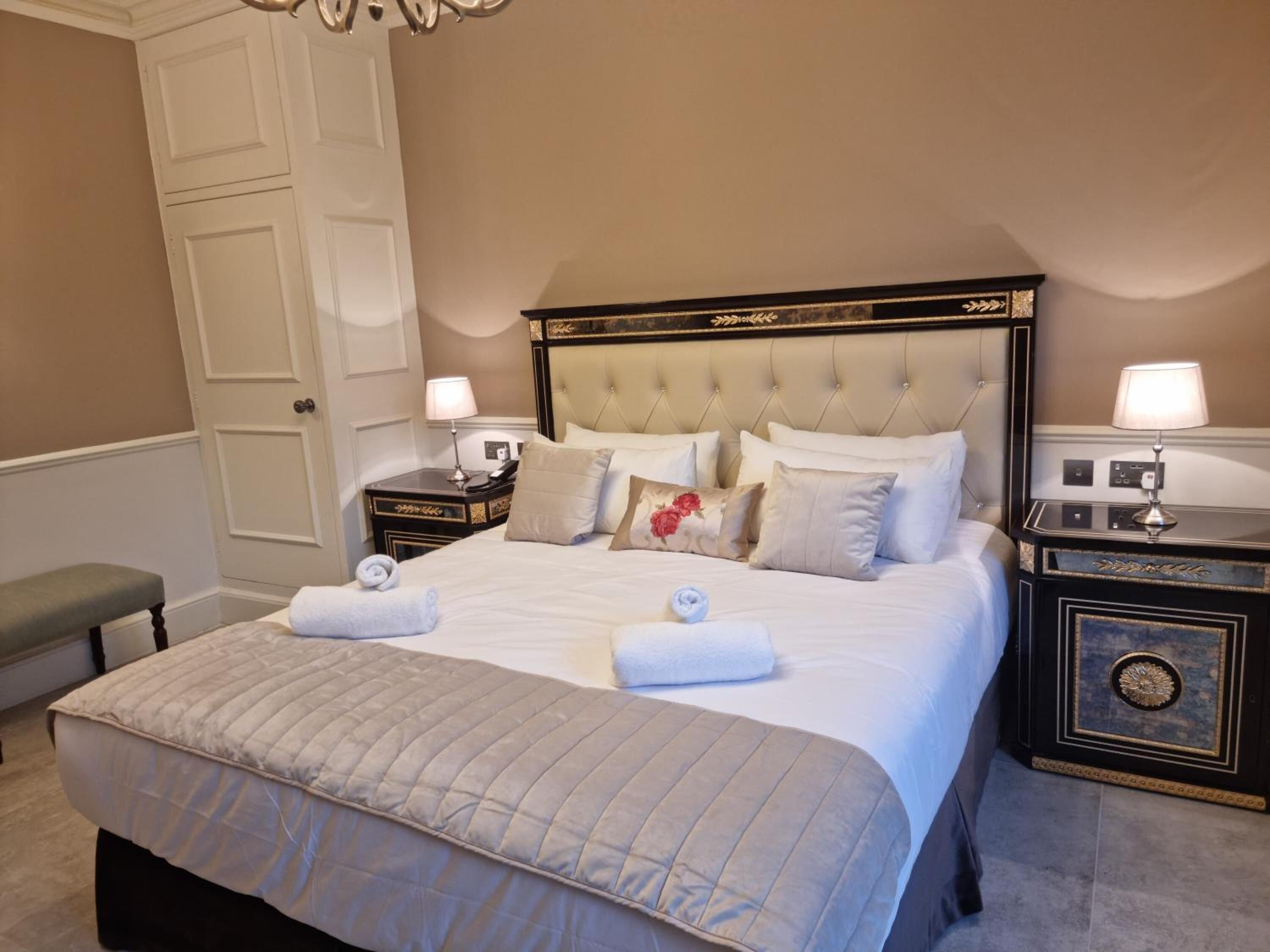 A neatly arranged bedroom with a large bed, two bedside tables, a bench, and a door.