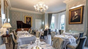 A formal dining room with tables set for service, a grand piano, and elegant wall decorations. - Weston Manor (Bicester)