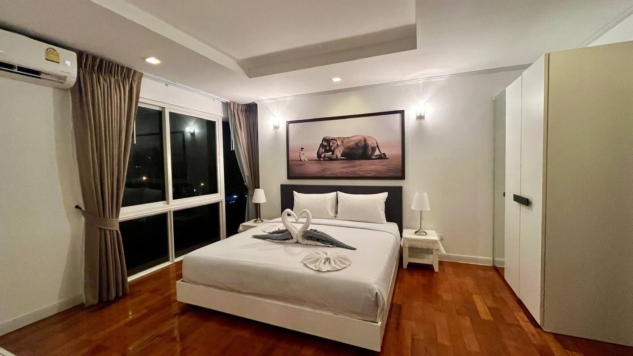 Une chambre d’hôtel avec un grand lit, un tableau représentant un éléphant endormi, une table de chevet et une armoire.