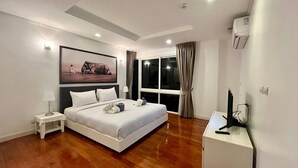 Une chambre d’hôtel moderne avec un grand lit, une table de chevet, un bureau avec un ordinateur, une grande fenêtre avec des rideaux et un tableau au mur.