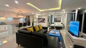 Un salon moderne avec un canapé noir, un coin repas et une cuisine.