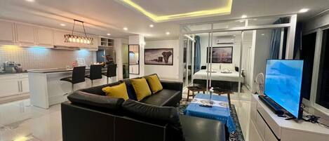 A modern living room with a black sofa, a dining area, and a kitchen.