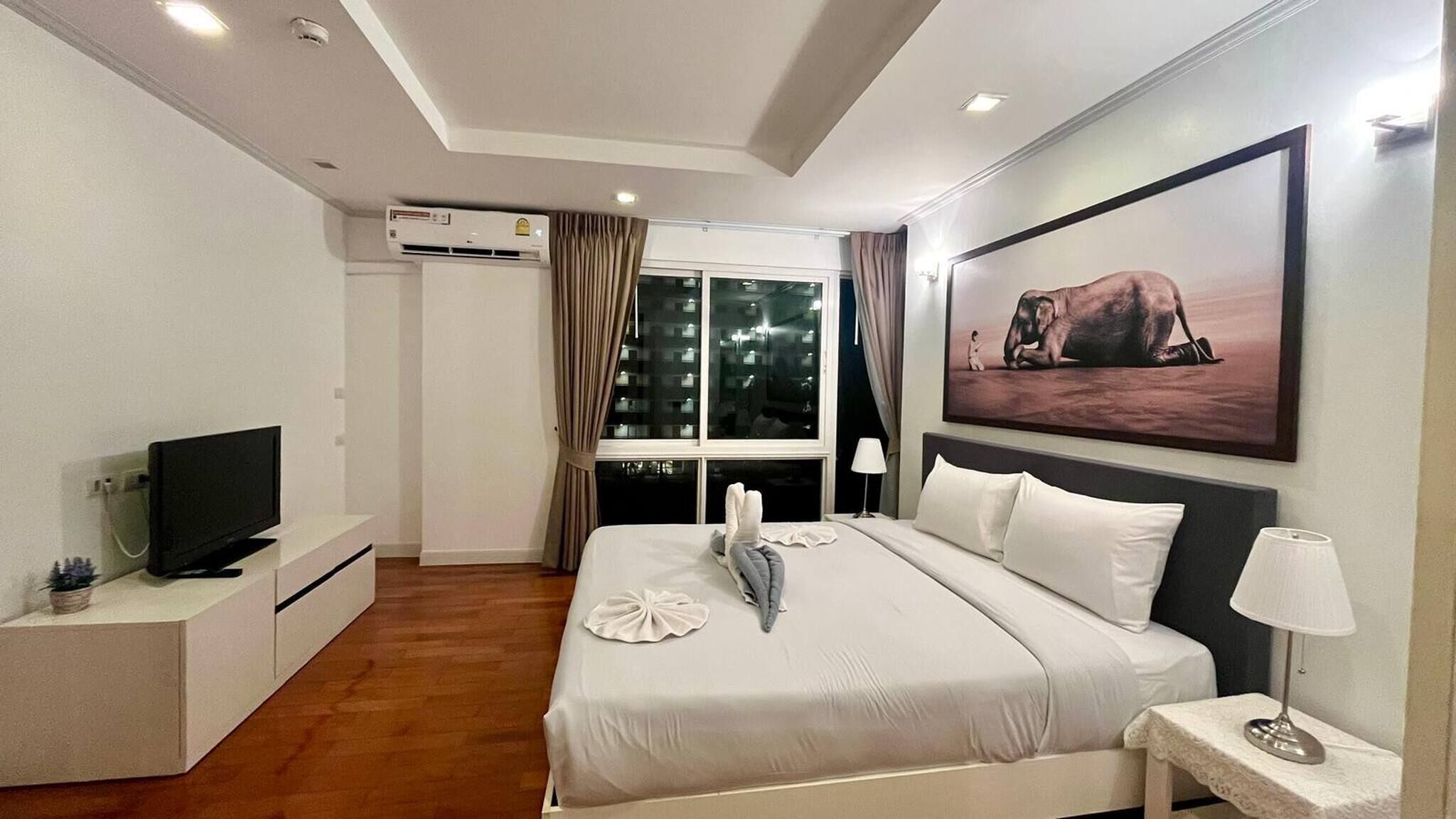 Ein modernes Hotelzimmer mit einem großen Bett, einem Flachbildfernseher, einem Fenster mit Vorhängen und einem Bild an der Wand.