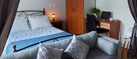 A bedroom with a bed, a sofa, a desk with a computer, a wardrobe, and a painting on the wall.