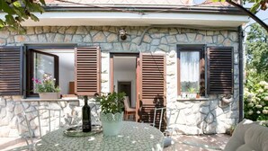 A stone house with a patio, a round table with a floral tablecloth, and a white cushioned chair. - Green Garden Oasis (Opatija)