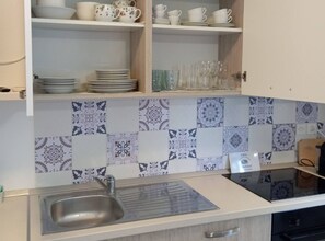 A kitchen with a tiled backsplash, a sink, and cabinets above. - Green Garden Oasis (Opatija)