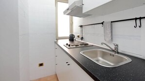 Una cuina moderna amb armaris blancs, un taulell negre, un rentaplatets d'acer inoxidable i una finestra que deixa entrar llum natural.