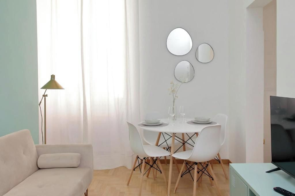 Ein modernes Wohnzimmer mit einem weißen Sofa, einem Esstisch mit Stühlen, einem Fernseher und einer Lampe.
