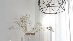 Habitació minimalista amb una taula de fusta, una làmpada geomètrica i un ram de flors seques.