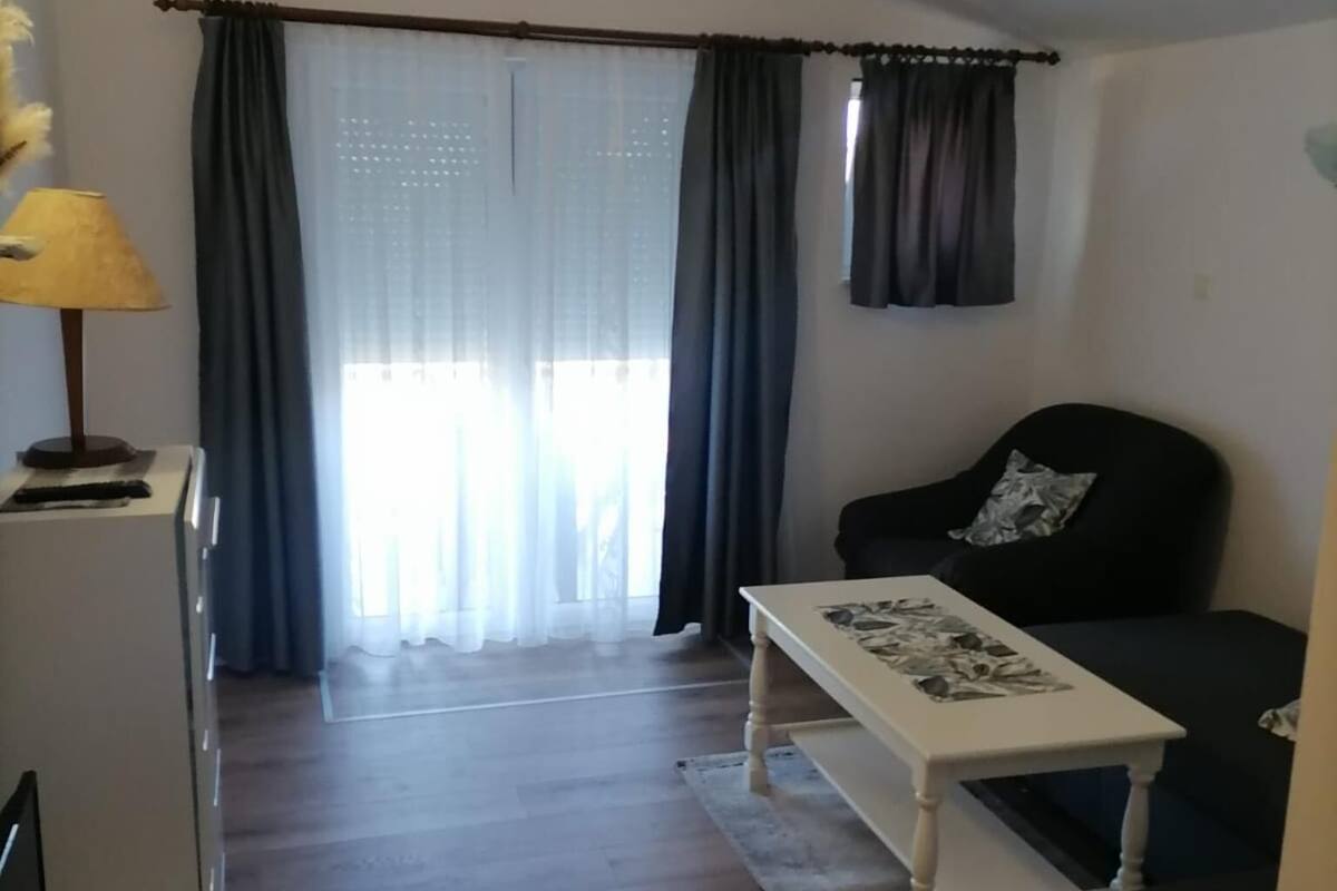 Un salon avec un canapé, une table basse et une lampe. Il y a une fenêtre avec des rideaux et une vue sur l’extérieur.