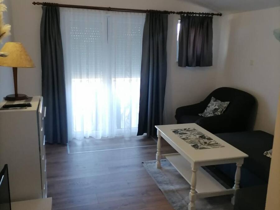 Een woonkamer met een bank, een bijzettafeltje en een lamp. Er is een raam met gordijnen en uitzicht.