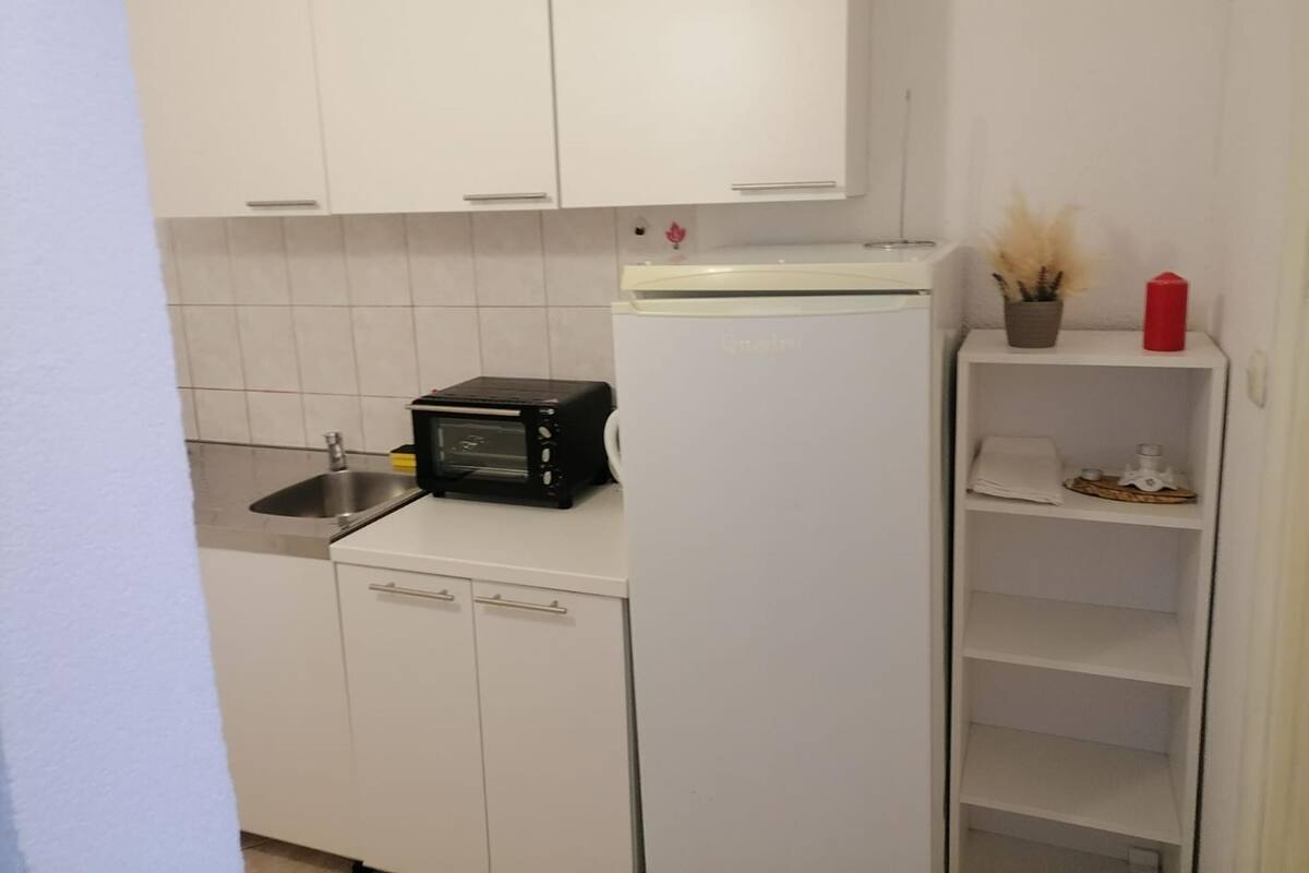 Une petite cuisine équipée avec des meubles blancs, un four grille-pain noir, un réfrigérateur blanc et un évier.