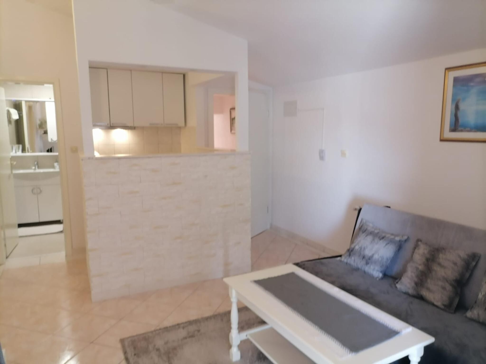 A living room with a grey sofa, a white coffee table, and a kitchen area with white cabinets.