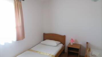Una cama individual con cabecera de madera, una mesita de noche con una lámpara rosa y un pequeño estante.