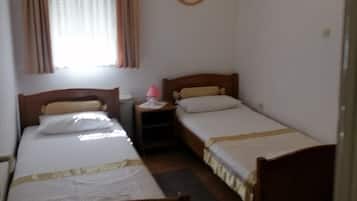 A small, simple room with two single beds, a nightstand, a lamp, and a window with curtains.