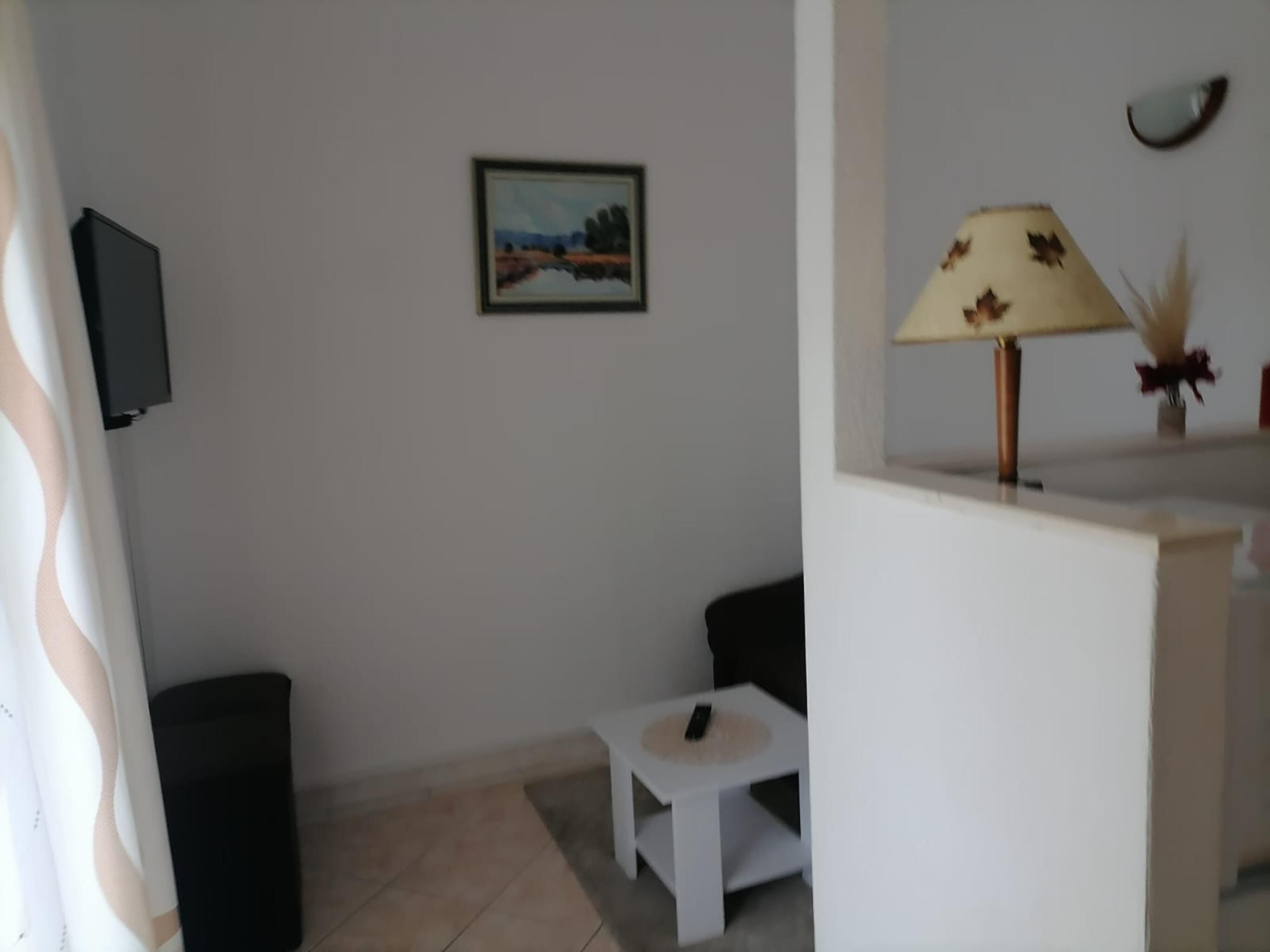Un salon avec un téléviseur fixé au mur, une petite table blanche et une lampe dotée d’un pied décoratif.